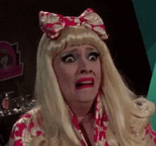 a woman in a wig with a bow on her head is making a funny face while holding a can of soda .