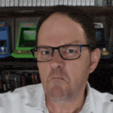 a man wearing glasses is making a funny face in front of an arcade machine .