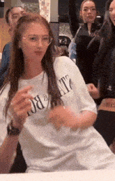 a woman wearing a white t-shirt with the word state on it stands in a crowd of people
