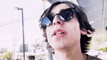 a young man wearing sunglasses looks at the camera with his mouth open .
