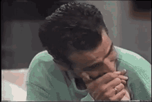 a man in a green sweater is smoking a cigarette while covering his mouth with his hands .