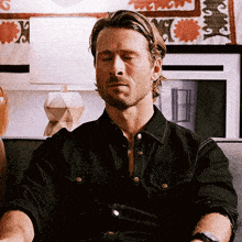 a man is sitting on a couch with his eyes closed . he is wearing a black shirt .