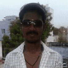 a man wearing sunglasses and a plaid shirt is standing in front of some buildings