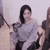 a woman in a gray sweater is sitting in a chair with another woman .