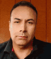 a close up of a man 's face with a wooden wall in the background