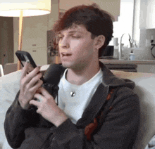 a young man is sitting on a couch holding a cell phone
