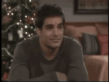 a man is sitting on a couch in front of a christmas tree in a living room .