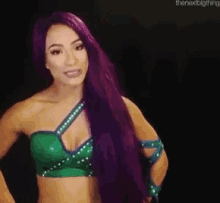 a woman with long purple hair is wearing a green top and a green bra .