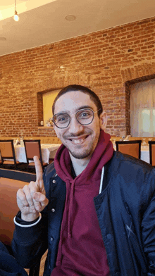 a man wearing glasses and a maroon hoodie is giving the peace sign