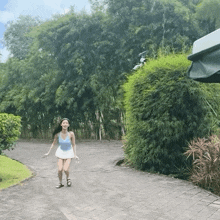 a woman in a blue tank top and white skirt is walking down a brick road