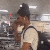 a man wearing ear buds is standing in a school cafeteria talking on a cell phone .