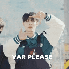 a young man in a varsity jacket is making a peace sign with his hands in front of a sign that says var please .