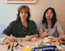two women sitting at a table with a box of reynolds wrap in front of them