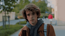 a young man with curly hair is wearing a brown jacket and a grey hoodie