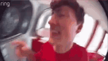 a man in a red shirt is looking through a fisheye lens .