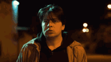 a man in a brown jacket is standing in front of a street light at night