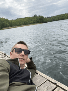 a man wearing sunglasses laying on a wooden dock overlooking a lake