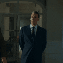 a man in a suit and tie is standing in a hallway with his hands in his pockets