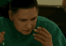 a woman in a green shirt is sitting at a table with her hand on her nose .