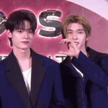 two men in suits are standing next to each other and one is making a heart shape with his hands