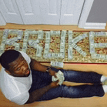 a man is laying on the floor holding a bunch of money in front of a rug that says ' i love you '