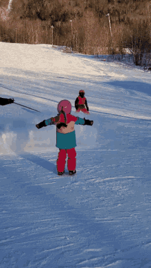 a little girl wearing a pink helmet is skiing down a snowy hill