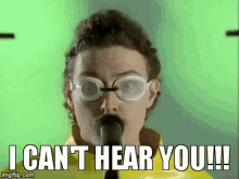 a man wearing goggles is singing into a microphone and says " i can 't hear you !!! "