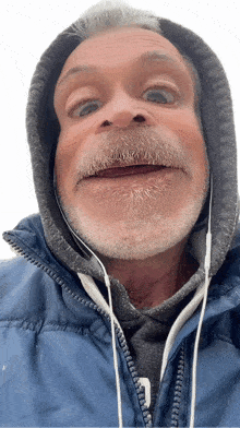 a man with a beard wearing a blue jacket and headphones making a funny face