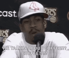 a man wearing a baseball cap is talking into a microphone and saying `` we talkin about coffee ? ''