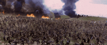 a large group of soldiers are running in a field with smoke coming out of a building in the background