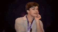 a young man with a purple lanyard around his neck is smiling and holding his hand to his chin .