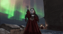 a little girl in a red dress is standing in front of a northern lights display