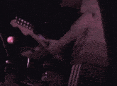 a man in a purple shirt is playing a guitar in a dark room