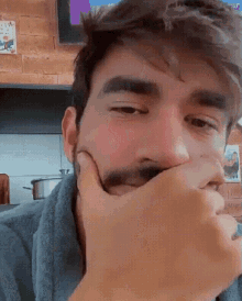 a man with a beard is covering his mouth with his hand in a kitchen .