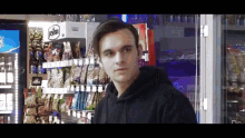 a man in a black hoodie is standing in front of a vending machine .