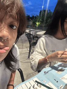 a girl wearing a white shirt that says ' t2h ' on it sits at a table