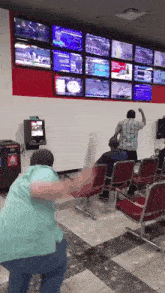 a man in a blue shirt is standing in front of a wall with lots of monitors