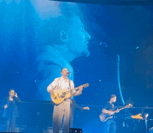 a man singing into a microphone while playing a guitar on stage