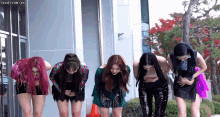 a group of women are kneeling down in front of a building with their hands on their stomachs .