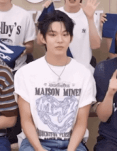 a man wearing a maison miney t-shirt sits in a crowd of people