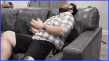 a man in a plaid shirt is laying on a couch with a green bottle in his hand