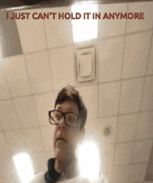 a man wearing glasses is looking at himself in a mirror with the words i just can 't hold it in anymore