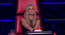 a woman is sitting in a red chair with a red button on her desk .