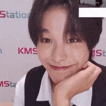 a woman is smiling with her hand on her chin in front of a sign that says kms