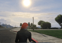 a woman with red hair is walking down a sidewalk with the sun shining brightly behind her