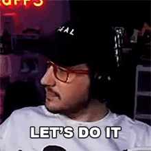 a man wearing headphones and a hat is sitting in front of a microphone and says let 's do it .