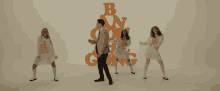 a man and three women are dancing in front of a wall with the letters b and n stacked on top of each other