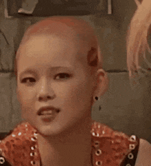 a young girl with a shaved head is wearing earrings and a red top .
