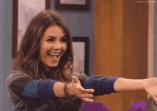 victoria justice is smiling and giving a thumbs up while holding a purple flower .