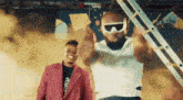 a man wearing sunglasses is standing next to another man .